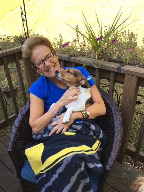Woman in blue shirt sitting outside smiles as she holds her beagle.