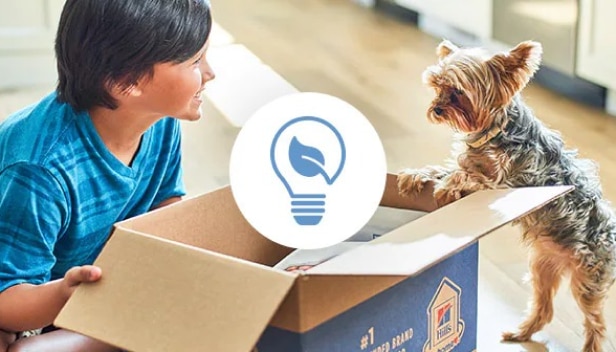A young boy and a dog looking at recyclable Hill’s box with a reducing waste icon on it
