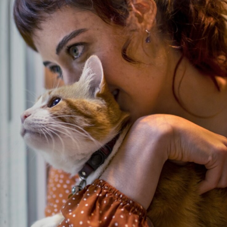 Woman in orange sweater holding a pet cat